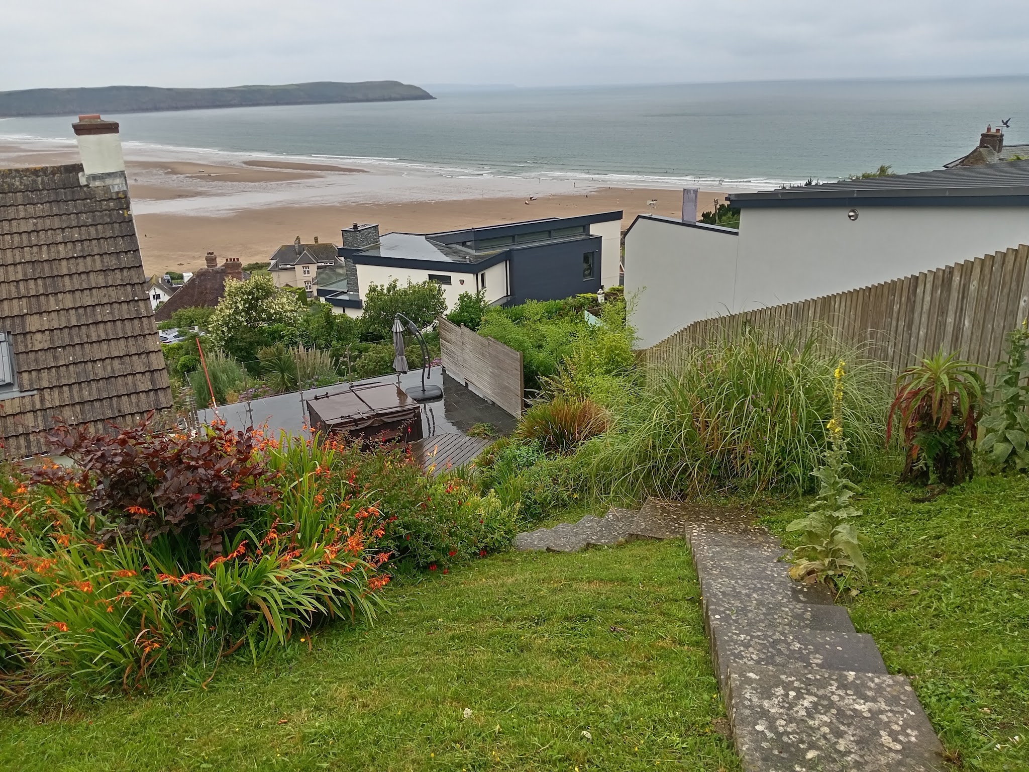 A sloping North Devon garden with crocosmia borders looking out over a wide beach and the sea