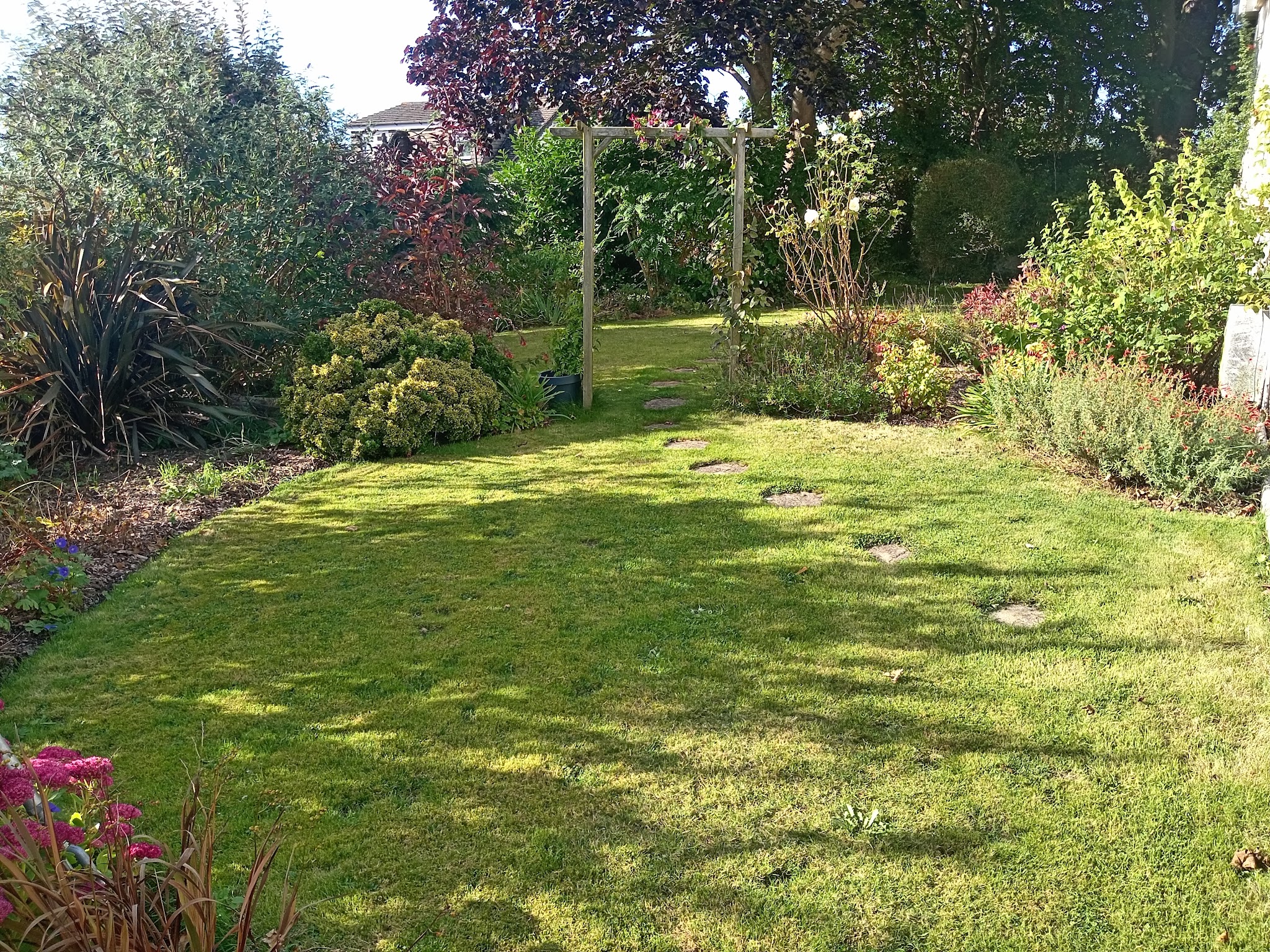 A neat curved lawn with stepping stones, a wooden arch and mixed borders